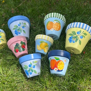以下が含まれることがあります： さまざまなデザインで手描きされたセラミックの花瓶が8つあります。花瓶には、青と白のストライプ、レモン、イチゴ、ブルーベリー、オレンジが描かれています。