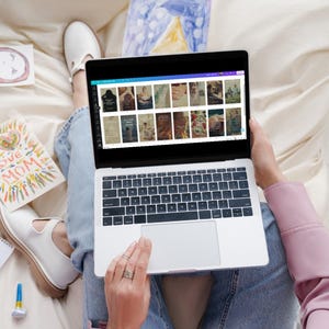 May include: A person sitting on a white couch using a laptop computer. The laptop screen shows a website with multiple images of different designs. The person is wearing blue jeans and a pink shirt.