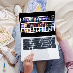 May include: A person is sitting on a bed with a laptop computer open. The laptop screen displays a grid of colorful images. The person is using their finger to scroll through the images.