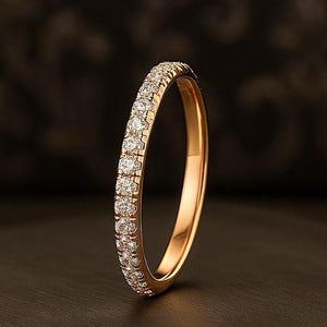 以下が含まれることがあります： 小さな透明な宝石が並んだゴールドリング。暗い背景にセットされ、石の輝きを際立たせています。様々な場面に適した、クラシックなデザインです。