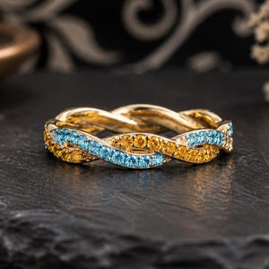 Peut inclure: Une bague en or au design torsadé, ornée de rangées alternées de petites pierres précieuses rondes bleu clair et jaunes serties sur toute la circonférence de l'anneau métallique, créant un aspect tressé continu.