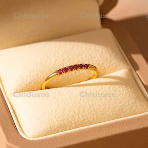 May include: A gold ring with a row of small, round, red gemstones. The ring is set in a beige jewelry box. The brand name "Chicluxee" is printed on the box.