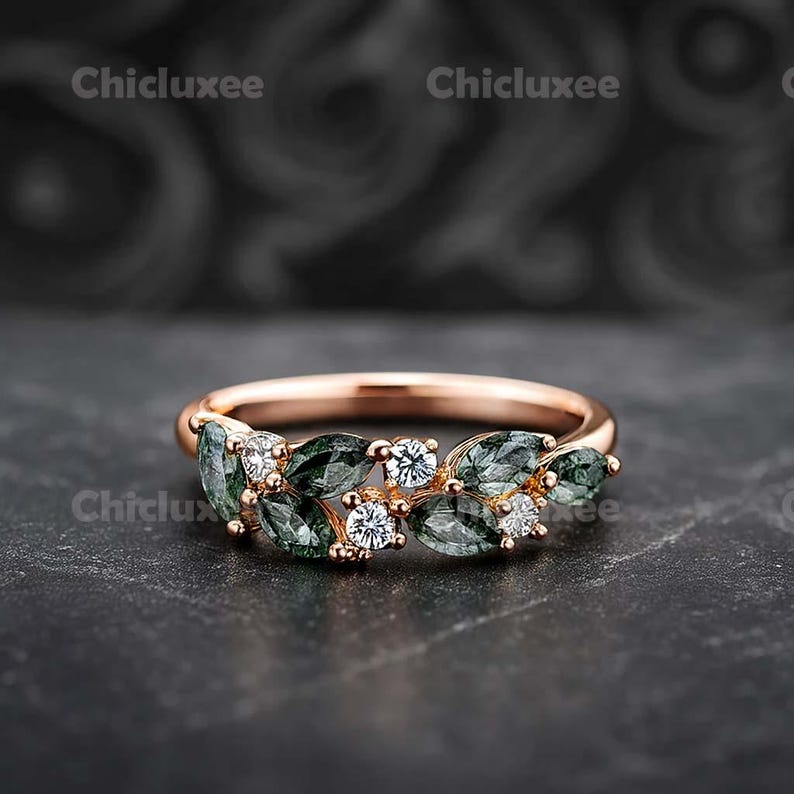 May include: Rose gold ring featuring a leaf design with green and white gemstones. The ring has a delicate band and is adorned with marquise-cut green stones and round white stones. The ring is displayed on a dark surface.