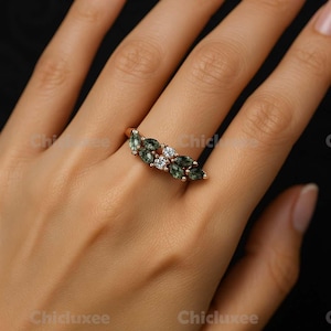 May include: A rose gold ring featuring a cluster of green marquise-cut gemstones and small white gemstones. The ring is displayed on a hand against a dark background. The brand name "Chicluxee" is visible in the image.