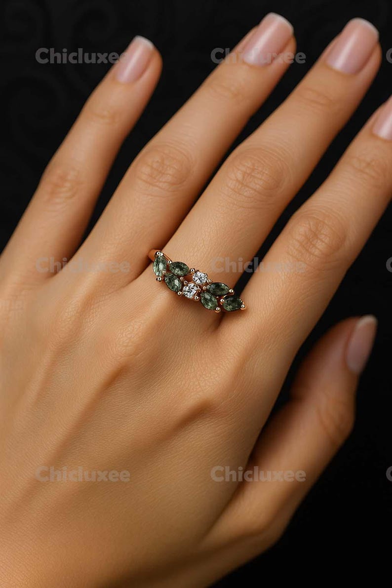 May include: A rose gold ring featuring a cluster of green marquise-cut gemstones and small white gemstones. The ring is displayed on a hand against a dark background. The brand name "Chicluxee" is visible in the image.