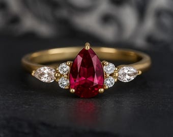 May include: A gold ring with a large, pear-cut, deep red gemstone as the focal point. The ring is embellished with smaller, round and marquise-shaped white gemstones. The band is plain, polished gold.