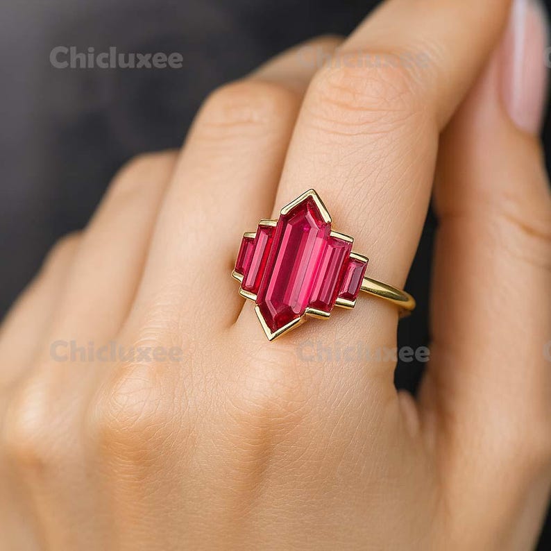 May include: A gold ring with a geometric design featuring a large, rectangular, ruby-red gemstone. The ring has a gold band and a decorative setting around the gemstone. The brand name "Chicluxee" is visible in the image.