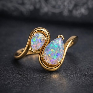 May include: A gold ring featuring two pear-shaped opal gemstones. The opals display a vibrant play-of-color, set in a swirling gold band. The ring is displayed on a dark surface, highlighting the jewelry's details.