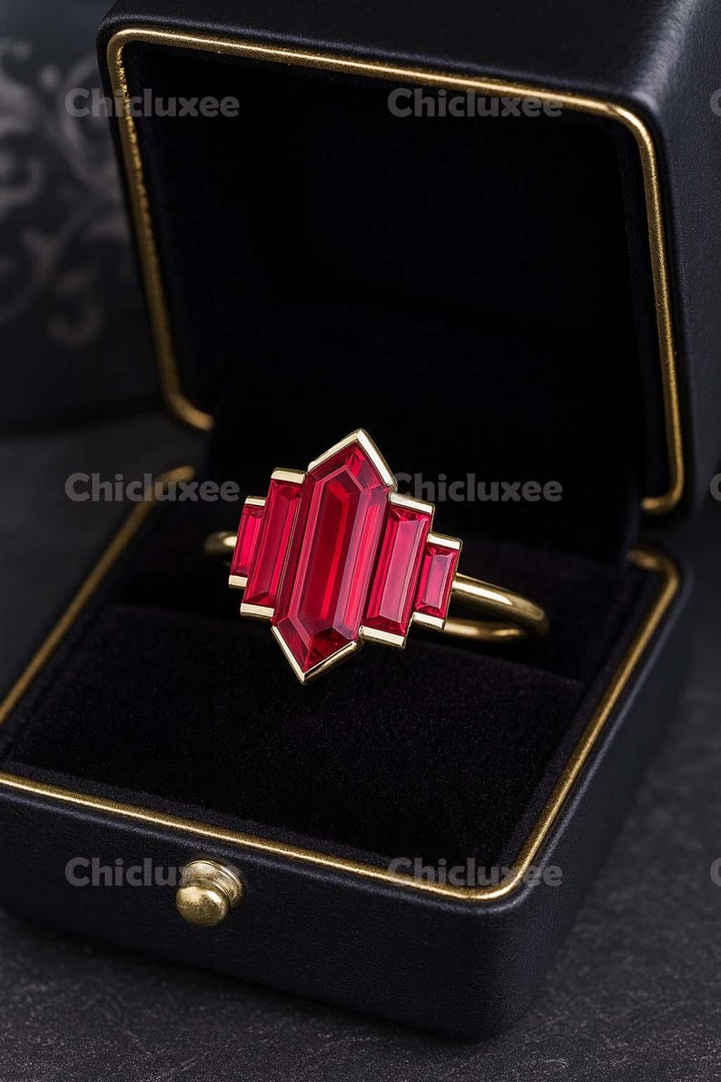 May include: A gold ring with a large, rectangular, ruby-red gemstone in a geometric design. The ring is set in a gold band and is displayed in a black jewelry box with a gold trim. The brand name "Chicluxee" is visible.