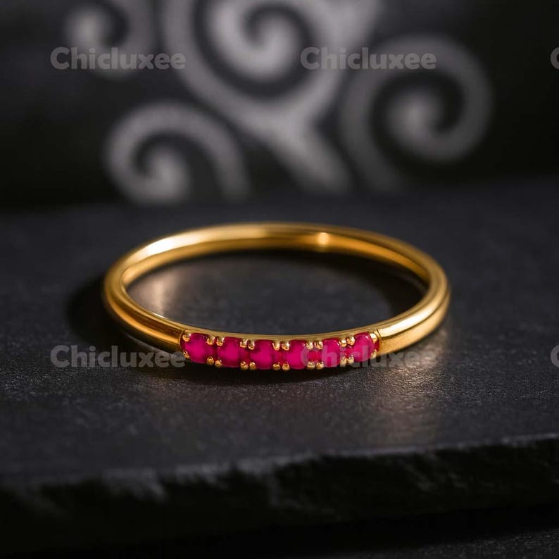 May include: A gold-colored ring with a row of bright pink gemstones. The ring is set against a dark background. The brand name "Chicluxee" is visible in the image.