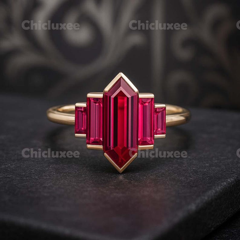 May include: A gold ring featuring a large, rectangular, deep red gemstone at the center, flanked by smaller rectangular stones. The ring has a geometric design and is set against a dark background. The word "Chicluxee" is printed in white in the corners.