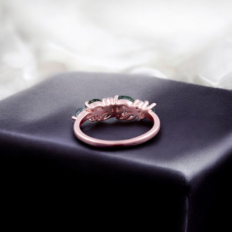 May include: A rose gold ring with a floral design, featuring green gemstones. The ring is set on a dark surface, with a soft, white background. The ring's intricate details and color contrast are highlighted.
