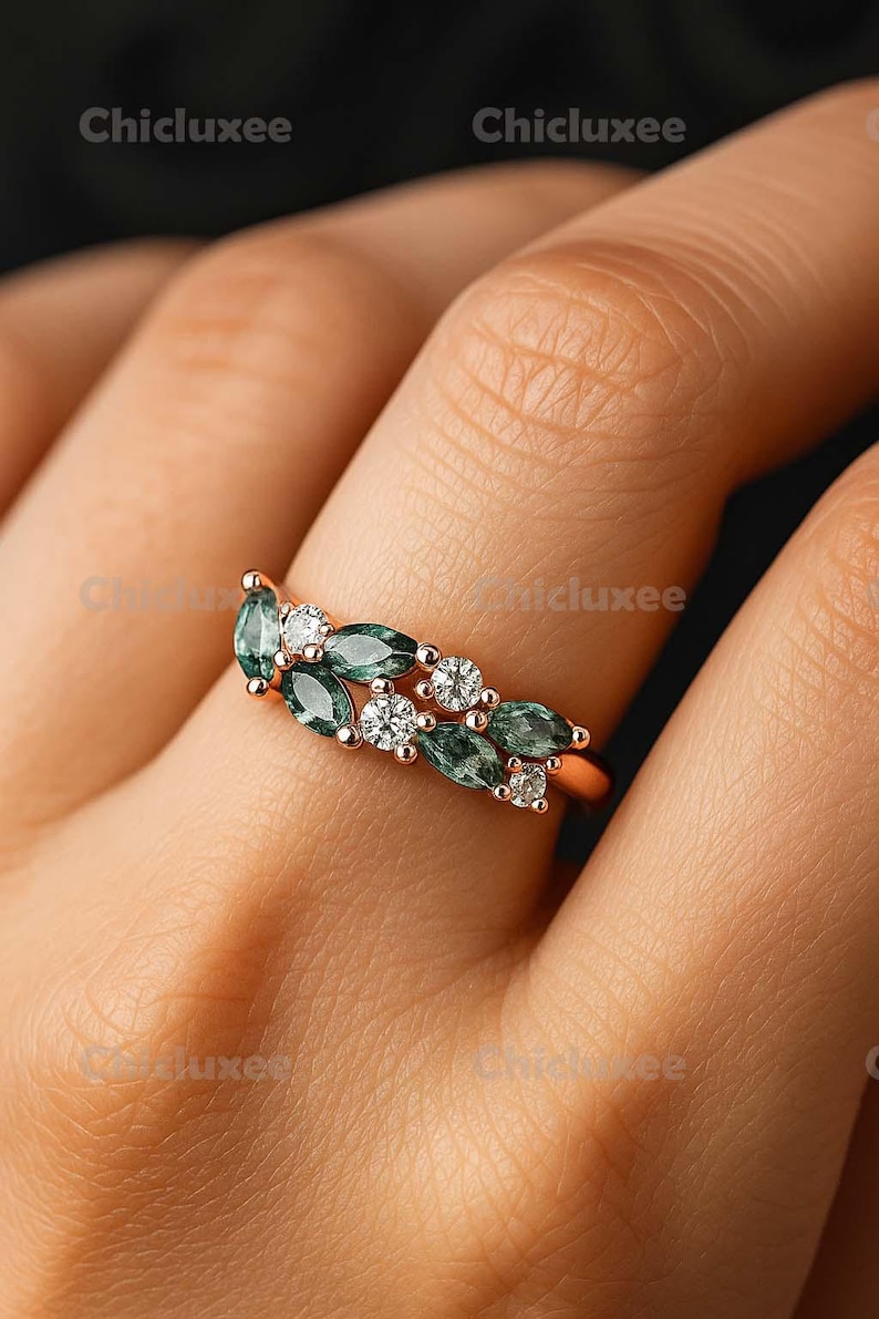 May include: A rose gold ring featuring a leaf-like design with alternating green and white gemstones. The ring's design incorporates marquise-cut green stones and round, clear stones, creating a nature-inspired aesthetic.