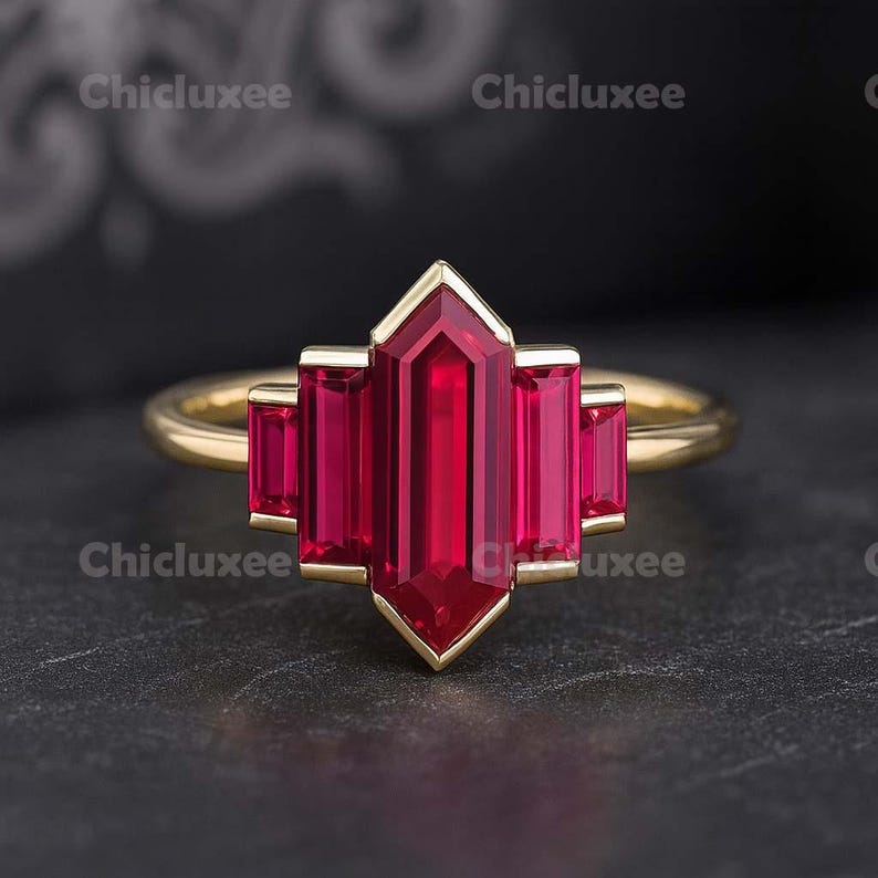 May include: A gold ring featuring a central, vibrant red gemstone in a geometric design. The ring's band is a simple gold, complementing the bold red of the gemstone. The gemstone is surrounded by a gold setting.