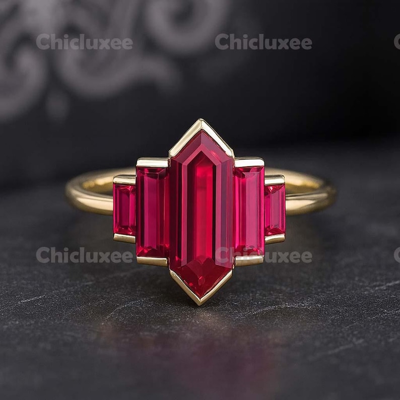 May include: A gold ring featuring a central, vibrant red gemstone in a geometric design. The ring's band is a simple gold, complementing the bold red of the gemstone. The gemstone is surrounded by a gold setting.