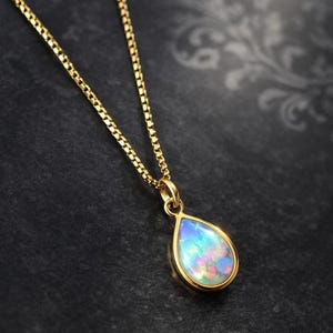 Op de afbeelding: Een gouden ketting met een druppelvormige hanger. De hanger heeft een kleurrijke opaalsteen met tinten blauw, groen en roze. De ketting is een delicaat gouden schakelontwerp en de hanger is gezet in een gouden rand.