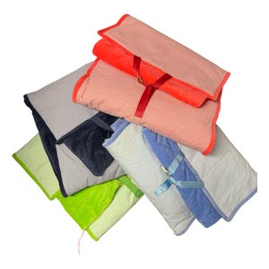 May include: A stack of folded baby blankets in various colors, including red, blue, green, and navy. Each blanket features a striped pattern and is trimmed with a contrasting color. Some are tied with ribbons.