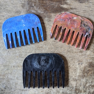 May include: Three combs made of colorful, marbled plastic. The combs are blue, orange and black. Each comb has a rounded top and seven teeth.