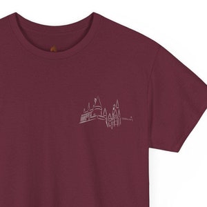 Puede incluir: Una camiseta color granate con un contorno blanco de un edificio en el pecho izquierdo.