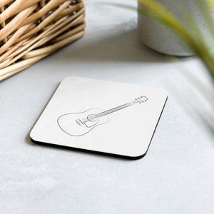 May include: A white square coaster with a black line drawing of an acoustic guitar.