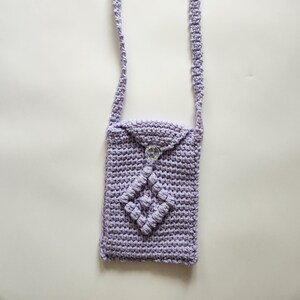 May include: A lavender crocheted crossbody bag with a decorative diamond-shaped design and a clear button closure.