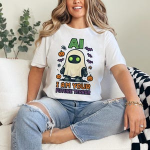 Puede incluir: Camiseta blanca con un diseño de Halloween. El diseño presenta una figura fantasmal con el texto "AI I AM YOUR FUTURE TERROR". La camiseta también incluye imágenes de calabazas y murciélagos.