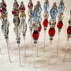 May include: A collection of decorative hat pins with silver-toned metal shafts. The pins feature various colorful bead designs, including red, blue, clear, and silver beads. The beads are arranged in decorative patterns.
