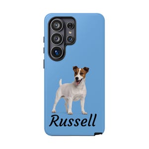 May include: A light blue phone case featuring a Jack Russell Terrier dog with brown and white markings. The dog is standing and has its tongue out. The name "Russell" is written in black script at the bottom of the case.