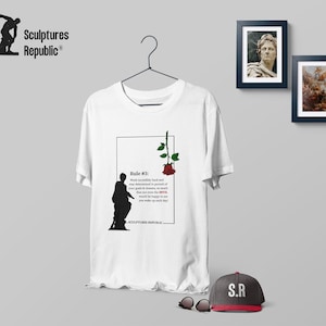 Puede incluir: Camiseta blanca con un gráfico en blanco y negro de una estatua y una rosa roja. El gráfico incluye el texto "Rule #3: Work incredibly hard and stay determined in pursuit of your goals & dreams, so much that not even the DEVIL would be happy to see you make up each day." -SCULPTURES REPUBLIC