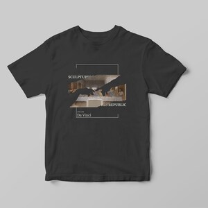 Puede incluir: Camiseta negra con un gr&aacute;fico blanco de dos manos que se alcanzan la una a la otra. El gr&aacute;fico es una imagen recortada de La &Uacute;ltima Cena de Leonardo da Vinci. El texto "SCULPTURE" y "THE REPUBLIC" est&aacute; por encima de la imagen y "Da Vinci" est&aacute; por debajo de la imagen.