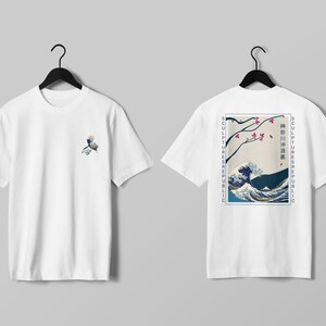 K&ouml;nnte beinhalten: Wei&szlig;e T-Shirts mit japanisch inspirierten Designs. Eines zeigt ein kleines Wellenmuster, das andere einen gr&ouml;&szlig;eren Druck einer Welle, Kirschbl&uuml;ten und Text. Beide Shirts h&auml;ngen an schwarzen Kleiderb&uuml;geln.