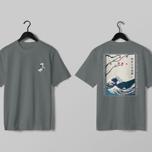 K&ouml;nnte beinhalten: Graues T-Shirt mit einem kleinen Wellenmuster auf der Vorderseite und einem gr&ouml;&szlig;eren japanischen Wellendesign auf der R&uuml;ckseite. Das R&uuml;ckendesign enth&auml;lt japanischen Text und die Worte "SCULPTURES REPUBLIC" vertikal auf beiden Seiten.