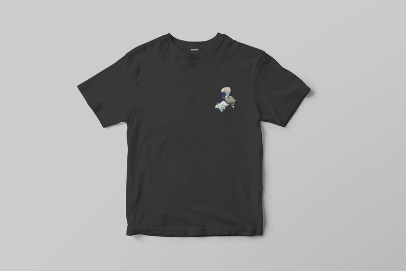 K&ouml;nnte beinhalten: Schwarzes T-Shirt mit einer kleinen, farbenfrohen Grafik auf der oberen linken Brustseite. Die Grafik ist eine stilisierte Illustration mit blauen, wei&szlig;en und grauen Elementen. Das T-Shirt wird vor einem hellgrauen Hintergrund pr&auml;sentiert.