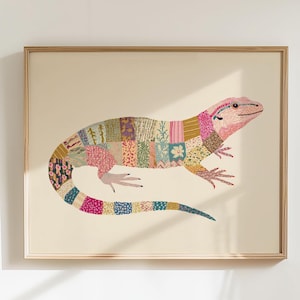 Puede incluir: Una impresión artística enmarcada con una ilustración de un lagarto colorido. El cuerpo del lagarto está compuesto por varios parches de tela estampada en tonos rosa, verde, azul y amarillo. La obra de arte está sobre un fondo crema.