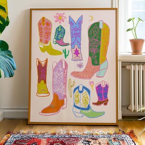 May include: A colorful illustration of cowboy boots in various styles and colors. The boots are arranged in a random pattern on a white background. The illustration is framed in a wooden frame.