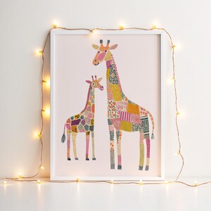May include: A framed art print featuring two giraffes with patchwork patterns in various colors. The giraffes stand on a light pink background, and the artwork is framed in a white border. Decorative string lights with small yellow bulbs are draped around the frame.