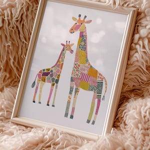 May include: A framed art print featuring two giraffes with patchwork-style patterns in various colors, including pink, yellow, and blue. The giraffes are set against a white background and framed in a light wood frame. The artwork is displayed on a fluffy, peach-colored surface.