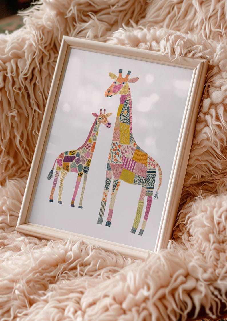May include: A framed art print featuring two giraffes with patchwork-style patterns in various colors, including pink, yellow, and blue. The giraffes are set against a white background and framed in a light wood frame. The artwork is displayed on a fluffy, peach-colored surface.