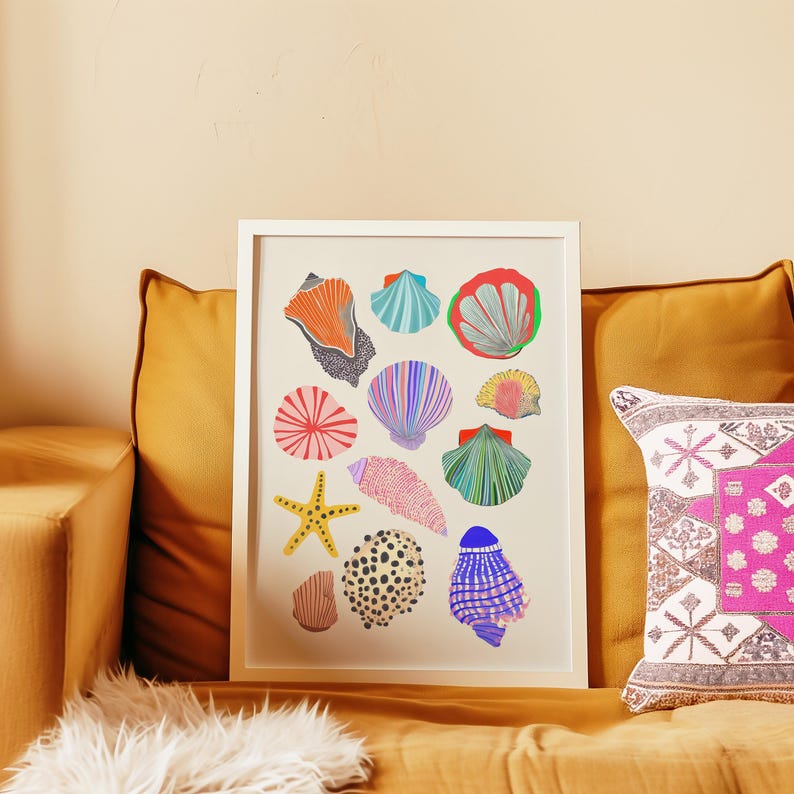 Puede incluir: Una impresi&oacute;n art&iacute;stica enmarcada con ilustraciones coloridas de varias conchas marinas. La obra de arte incluye una estrella de mar y varias conchas en tonos naranja, azul, rosa y verde. La impresi&oacute;n se muestra en un sof&aacute; color mostaza con cojines decorativos.