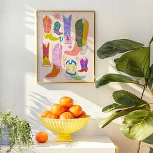 May include: A framed print of a colorful illustration of cowboy boots with a pink background. The boots are in various colors and patterns, including pink, blue, green, and yellow.
