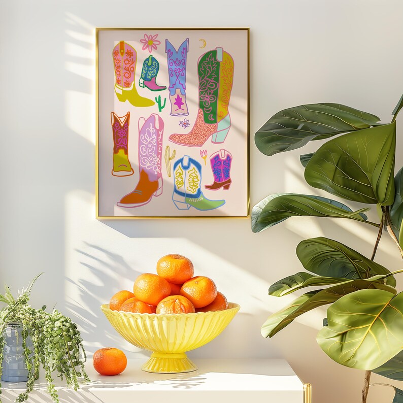 May include: A framed print of a colorful illustration of cowboy boots with a pink background. The boots are in various colors and patterns, including pink, blue, green, and yellow.