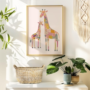 May include: A framed art print featuring two giraffes with patchwork patterns in various colors. The giraffes stand against a white background, framed in gold. A woven basket and potted plants are in the foreground.