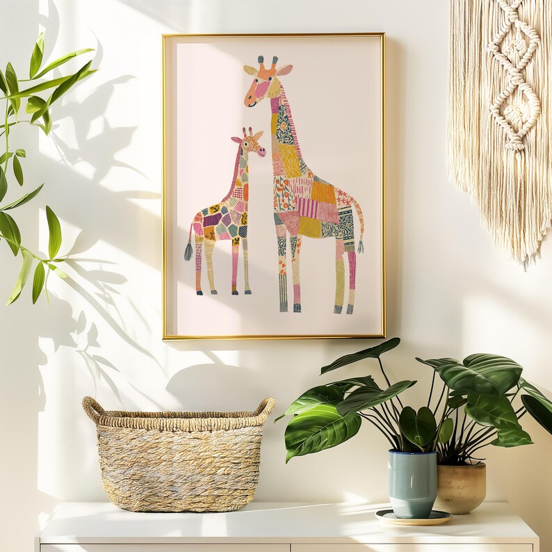 May include: A framed art print featuring two giraffes with patchwork patterns in various colors. The giraffes stand against a white background, framed in gold. A woven basket and potted plants are in the foreground.