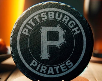 Peut inclure: Un dessous de verre rond en ardoise noire avec le logo des Pirates de Pittsburgh, présenté sur un support en bois. Le dessous de verre est gravé du nom et du logo de l'équipe en blanc. Deux verres de bière et une assiette de nourriture sont en arrière-plan.