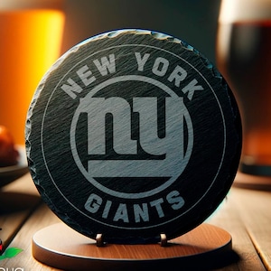 May include: A black slate coaster with a white New York Giants logo. The coaster is on a wooden stand and there are two glasses of beer in the background.