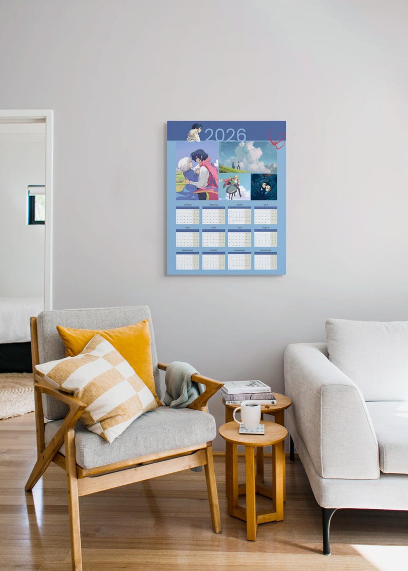 May include: A blue 2026 calendar featuring anime-style illustrations. The calendar is hanging on a gray wall above a gray armchair with yellow pillows. A small wooden side table with a mug and books is next to the chair.