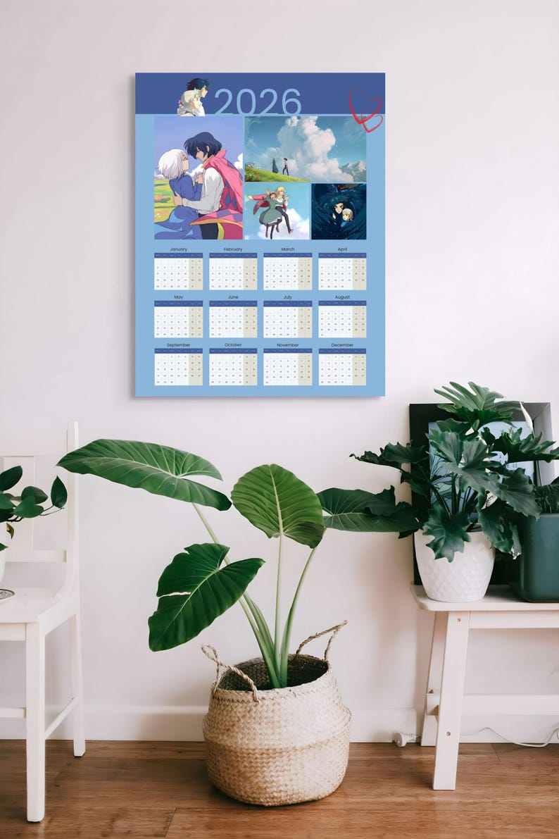 May include: A light blue 2026 calendar featuring anime-style illustrations. The calendar has a grid layout with dates and months. The top section includes several colorful images. The calendar is hanging on a white wall, with plants in the foreground.