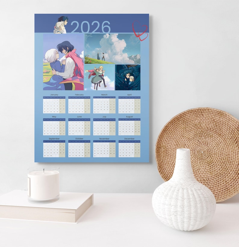 May include: A 2026 calendar featuring anime-style artwork. The calendar has a blue background with images and dates for each month. The top of the calendar has the year 2026 and a heart design. A white candle and vase are in the foreground.