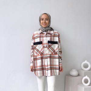 May include: A white and orange plaid flannel shirt with black trim on the pockets. The shirt has a button-down front and long sleeves.