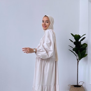 May include: A beige tiered maxi dress with long sleeves and a gathered neckline. The dress is made from a lightweight fabric and has a relaxed fit.